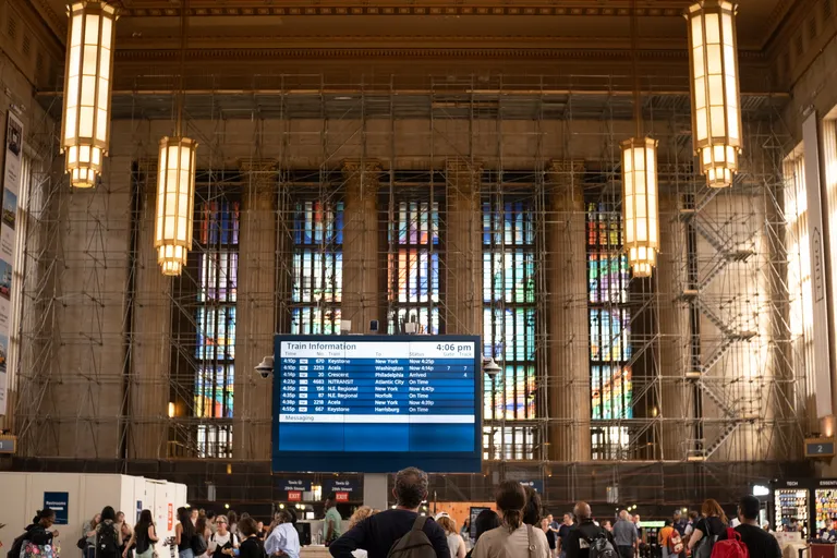 The inside east wall of the Amtrak area of 30th St station in Philadelphia, with scaffolding in front of it. The departures board is center of shot.