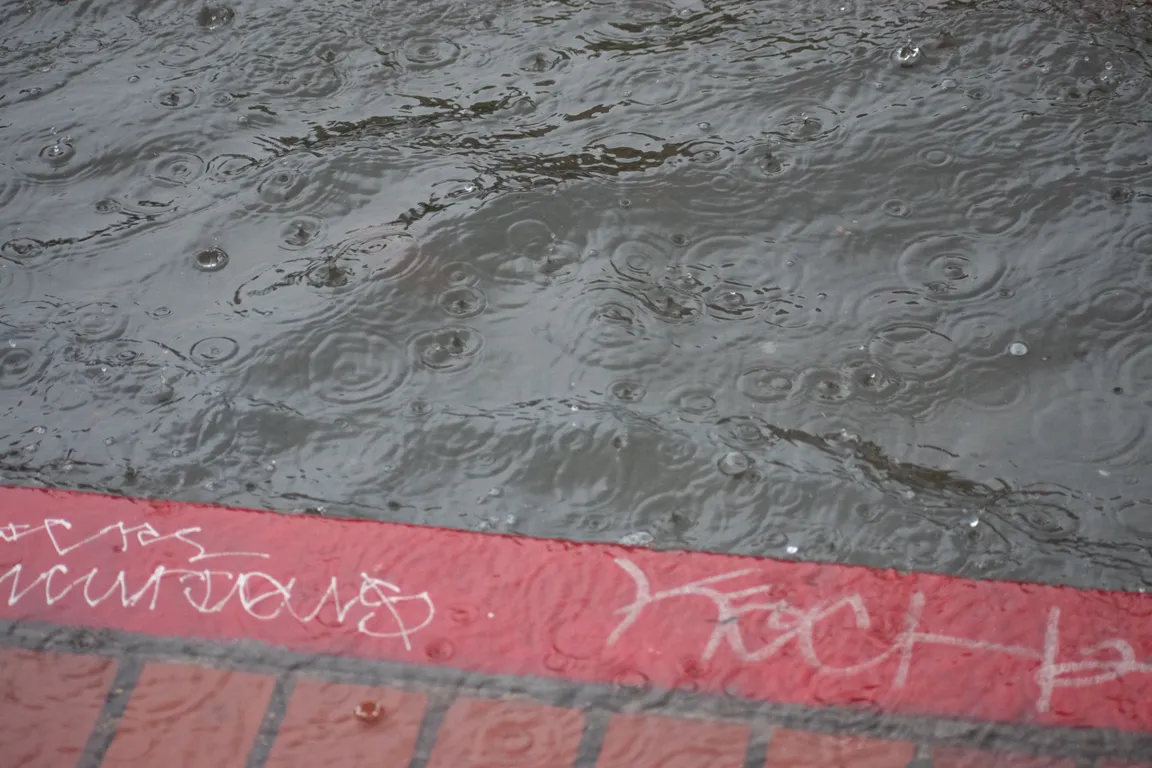 Rain flooding up against a red curb