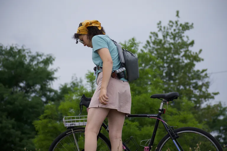 Natalie holds her bike, wearing a skirt and a crop top