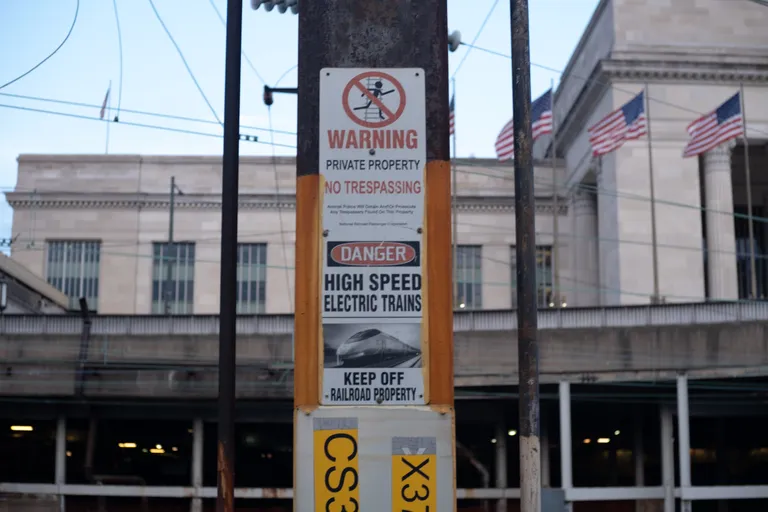 An oddly high definition sign with a motion-blur-y picture of the Acela reading “DANGER: HIGH SPEED TRAINS - KEEP OFF RAILROAD PROPERTY”